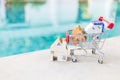 Wooden house model in shopping cart over blurred swimming pool water background, outdoor day light Royalty Free Stock Photo