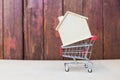 Wooden house model on shopping cart with space on blurred wood background, buy new house Royalty Free Stock Photo