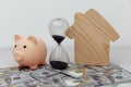 Wooden house, piggy bank and clock on dollar banknotes. Investment, savings and real estate