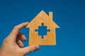 Wooden house from a puzzle and a hand on a background of blue sky. Royalty Free Stock Photo