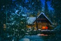 Wooden house with red light window near fir Christmas tree in winter Royalty Free Stock Photo