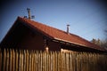 Wooden house with red tiled roof and blue sky. Fence made of sharp wooden stakes. Blurred