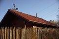 Wooden house with red tiled roof and blue sky. Fence made of sharp wooden stakes