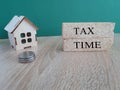 A wooden house sits next to a stack of brick blocks with the word Tax Time. Beautiful green background, wood table. Royalty Free Stock Photo