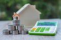 A wooden house on the table A pile of coins that are stacked high in a triangle And calculator The concept of saving money for