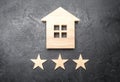 Wooden house and three stars on a gray background. Rating of houses and private property. Buying and selling, renting apartments. Royalty Free Stock Photo