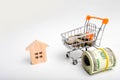 A wooden house and a trolley with money. The concept of buying a house and investing in repairs. Renovation of housing stock, inve