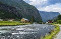 Wooden houses and clear river at the foot of a mountain covered with green grass. Summer scene in Norway Royalty Free Stock Photo