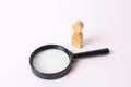 A wooden human figure stands near a magnifying glass on a white background. The concept of the search for people and workers. Royalty Free Stock Photo