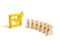 Wooden human figures stand together next to a yellow tick in the box. The concept of elections and social technologies. Volunteers Royalty Free Stock Photo