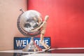 Wooden Human Manikin posing with an ornamental silver world globe and a blue welcome sign