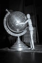 Wooden Human Manikin posing with an ornamental silver world globe and a blue welcome sign