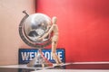 Wooden Human Manikin posing with an ornamental silver world globe and a blue welcome sign