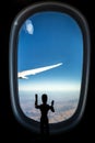 A Wooden Human Manikin standing looking through an airplane window at the landscape below