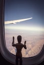 A Wooden Human Manikin standing looking through an airplane window at the landscape below