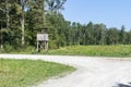 Wooden hunting post standing next to gravel path on the forest edge where wildlife go to graze the grass on the meadow behind near