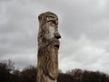 Wooden idol of the Slavic God Perun near the path in the forest. Gloomy forest in the background and dark clouds