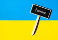 Wooden information label sign with text FAMINE against Ukrainian national flag message. Global hunger, inflation, high