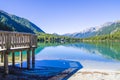 Wooden jetty on bright blue mountain lake under blue sky with woods, stones and snow Royalty Free Stock Photo