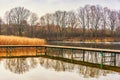 Wooden jetty at the lake surrounded by trees. Autumn landscape and reflection in the water. Royalty Free Stock Photo