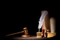 Wooden judge gavel hammer, old inkstand with feather quill, blotter, seal near scrolls against black background. Dramatic light.