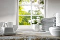 Wooden kitchen tabletop with white kitchenware and window with blurred plants and window  background. Royalty Free Stock Photo