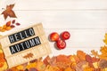 Wooden letter board with the text phrase Hello Autumn, three red ripe apples and dry fallen leaves on a white background Royalty Free Stock Photo