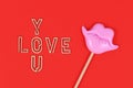 Wooden letters forming words `love you` next to photo prop in shapes of pink kiss mouth on red background