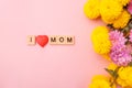 Wooden letters in the phrase I love mom with flowers on a pink background. Greeting card concept for mother day. Royalty Free Stock Photo