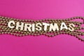 Wooden letters sign Christmas on goldean beads, pink background