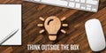 Wooden lightbulb symbol and text THINK OUTSIDE THE BOX with notepad, keyboard and mouse on wooden desk