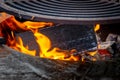 A wooden log burns brightly in a wood-fired grill. Circle wood-fired grill with steel grate for outdoor cooking