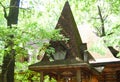 A wooden log hut with a patterned porch among green trees in the forest. An old log house among the trees. A porch with Royalty Free Stock Photo