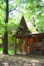 A wooden log hut with a patterned porch among green trees in the forest. An old log house among the trees. A porch with Royalty Free Stock Photo