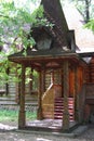 A wooden log hut with a patterned porch among green trees in the forest. An old log house among the trees. A porch with Royalty Free Stock Photo