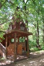 A wooden log hut with a patterned porch among green trees in the forest. An old log house among the trees. A porch with Royalty Free Stock Photo