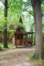 A wooden log hut with a patterned porch among green trees in the forest. An old log house among the trees. A porch with Royalty Free Stock Photo