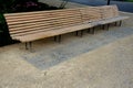 Wooden long park bench with curved backrest anatomical wooden cladding made of light wood on the ground light beige gravel, which