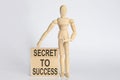 Wooden man shows with a hand text SECRET TO SUCCESS on wooden block