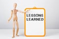 Wooden man shows with a hand to white board with text LESSONS LEARNED Royalty Free Stock Photo