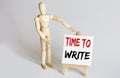 Wooden man shows with a hand to white easel with text TIME TO WRITE on white background