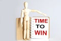 Wooden man shows with a hand to white notepad with text time to win Royalty Free Stock Photo