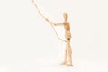 A wooden manequin toy holding holding a thin rope in his hand