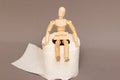 A wooden maniken sits on a roll of toilet paper labeled diarrhea, demanstrating bowel problems.