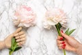 Wooden mannequin hand and female hand with piony flower on marble background