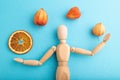 Wooden mannequin juggling dried citrus and physalis on blue pastel background. close up