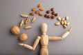 Wooden mannequin juggling nuts on gray pastel background. close up