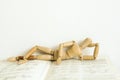 Wooden mannequin manikin lie down and rest on an open book.