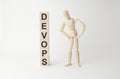 Wooden mannequin near tower of cubes with word devops on table against light background Royalty Free Stock Photo
