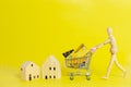 Wooden mannequin or puppet pushing shopping cart with credit card and wood house on yellow background.